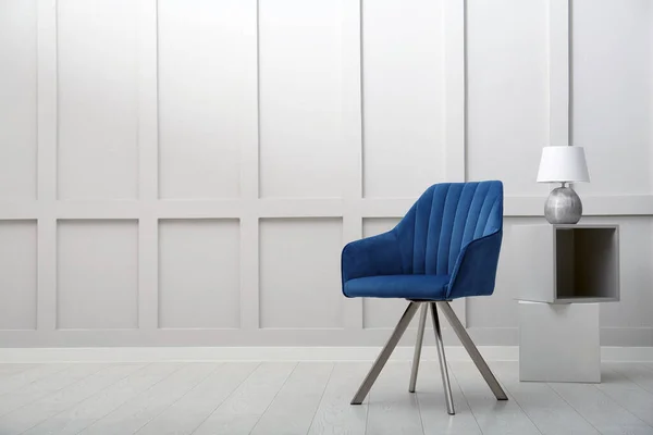 Modern blue armchair and lamp near white wall indoors. Space for text