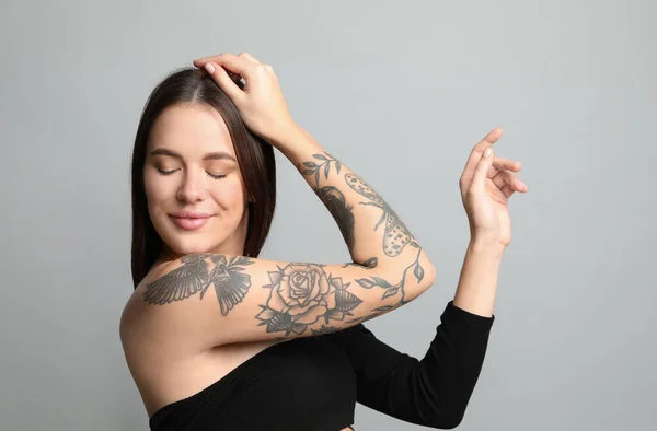 Vacker Kvinna Med Tatueringar Armen Mot Grå Bakgrund — Stockfoto