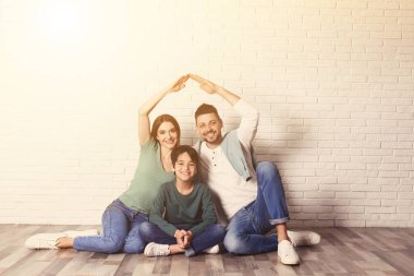 Elleri tuğla duvara yakın bir çatı oluşturan mutlu bir aile. Sigorta konsepti