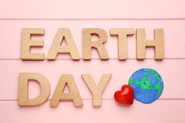 Words Earth Day, plasticine planet and decorative heart on pink wooden table, flat lay