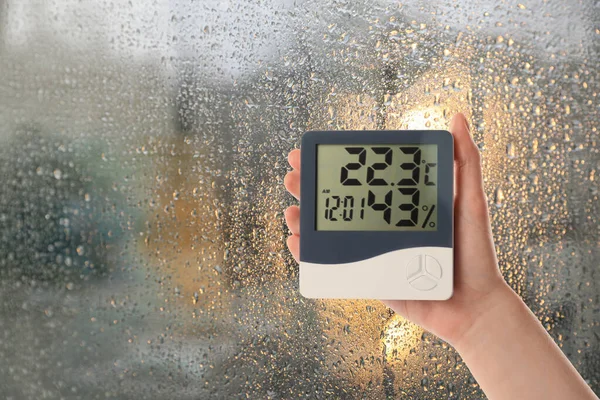 雨の日に窓の近くに温度計でデジタル湿度計を保持する女性 クローズアップ テキストのスペース — ストック写真