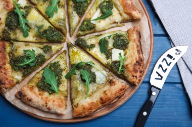 Mavi ahşap masada servis edilen pesto, peynir ve roka ile nefis bir pizza.