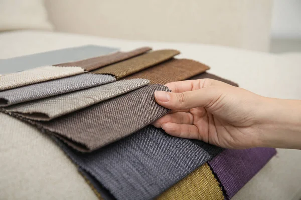 Woman choosing fabric among colorful samples on beige sofa, closeup