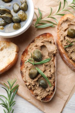 Lezzetli ezmeli ekmek dilimleri, kapari ve biberiye beyaz ahşap masada, düz yatıyordu.