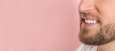 Pembe arka planda sağlıklı dişleri olan genç adamın yakın görüntüsü, mesaj için yer var. Pankart tasarımı
