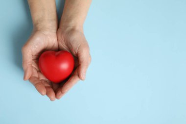 Açık mavi arka planda kırmızı kalbi elinde tutan yaşlı bir kadın. Metin için boşluk