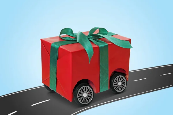 礼品盒上的车轮骑在沥青路面上 背景为浅蓝色 交付服务 — 图库照片