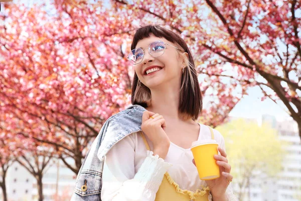 Piękna Młoda Kobieta Trzyma Papierowy Kubek Kawy Parku Kwitnącymi Drzewami — Zdjęcie stockowe