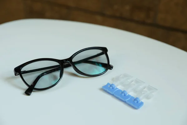 Single dose eye drops and glasses on white table