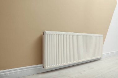 Modern radiator on beige wall indoors. Central heating system