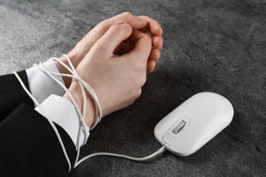 Gri masada eli bilgisayar faresi kablosuyla bağlanmış bir adam var. Yakın plan. İnternet bağımlılığı
