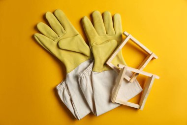 Sarı arka planda arıcılık eldivenleri ve bal peteği çerçeveleri, düz uzanmış.