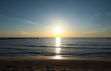 Gün batımında kumlu sahil ve denizin manzarası.