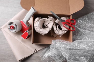 Paketlenmiş eşyalar, yapıştırıcı bant, makas, kağıt ve baloncuk ambalajlı kutuyu ahşap masaya aç, düz uzan