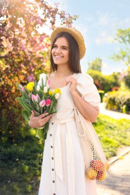 Güneşli bir günde bir buket lale ve elmayla parkta güzel bir genç kadın.