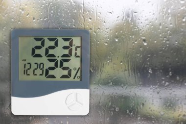 Digital hygrometer with thermometer on glass with water drops. Space for text clipart