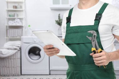 Banyoda boru anahtarı ve tableti olan bir tesisatçı, yakın plan. Metin için boşluk