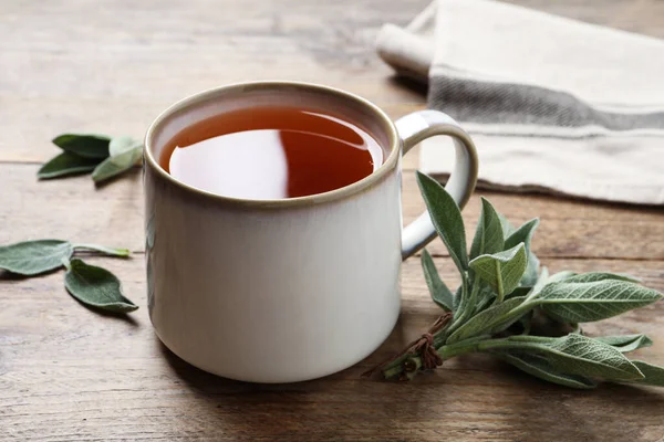 木のテーブルの上で香り豊かなセージ茶と新鮮な葉のカップ — ストック写真