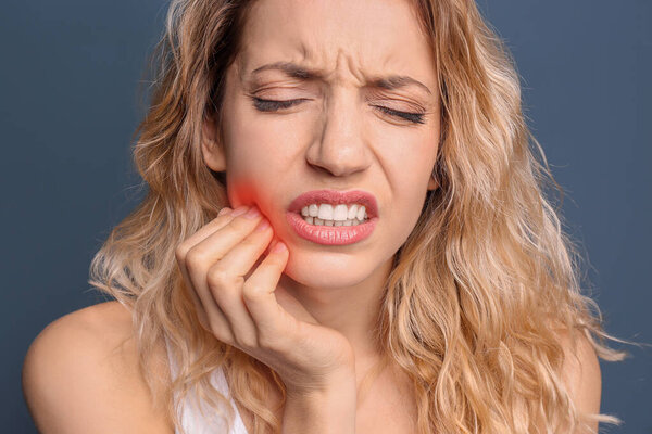 Young woman suffering from toothache on dark blue background