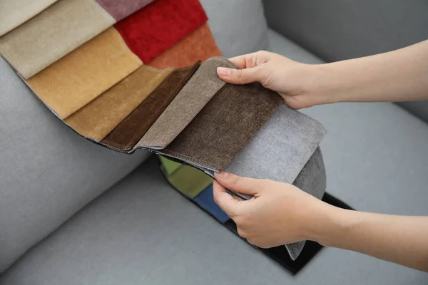Woman choosing fabric among colorful samples on grey sofa, closeup
