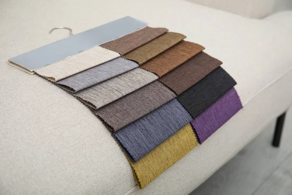 Catalog of colorful fabric samples on beige sofa, closeup