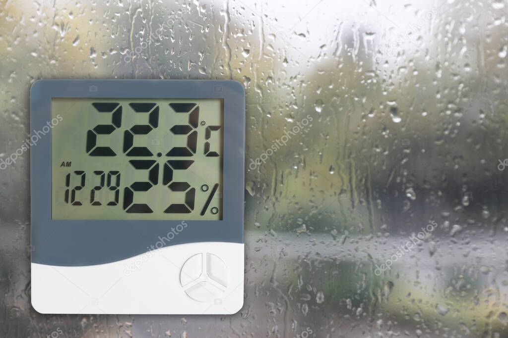 Digital hygrometer with thermometer on glass with water drops. Space for text