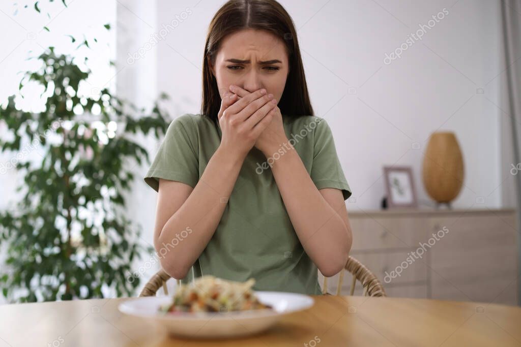 Young woman feeling nausea while seeing food at wooden table indoors