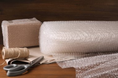 Makas, sicim, kağıt, yuvarlak baloncuk paketi ve tahta masaya paketlenmiş kutu.