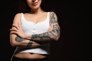Siyah arka planda kollarında dövmeleri olan güzel bir kadın, yakın plan. Metin için boşluk