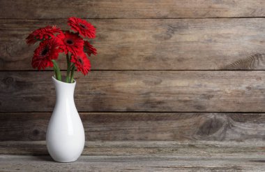 Ahşap masadaki seramik vazoda güzel kırmızı gerbera çiçekleri. Metin için boşluk