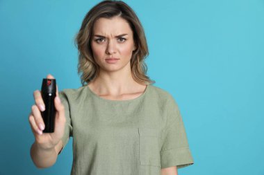 Turkuaz arka planda biber gazı kullanan genç bir kadın.