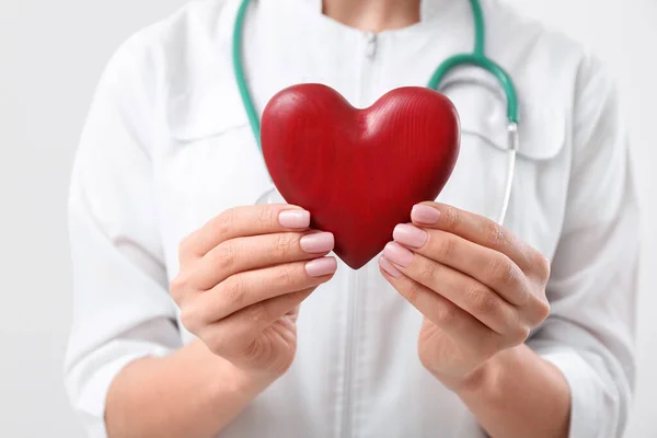 Doctor holding red heart on white background, closeup. Cardiology concept