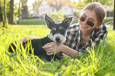 Parktaki yeşil çimlerde dinlenen sevimli köpeğiyle genç bir kız.