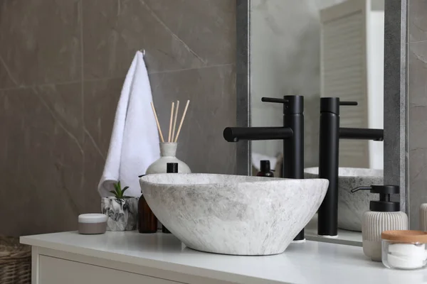 Stone vessel sink with faucet and toiletries on white countertop in bathroom