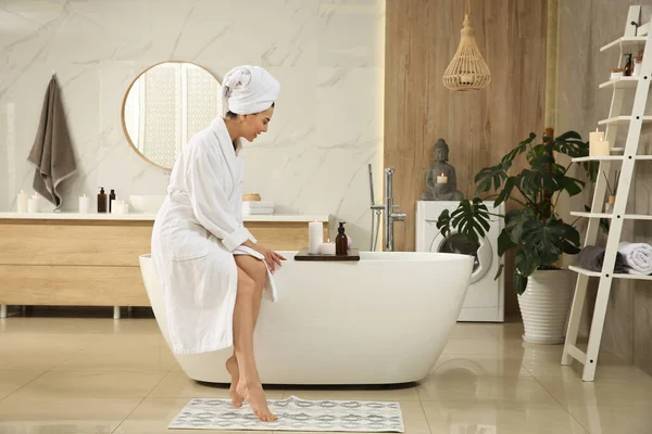 Beautiful young woman sitting on edge of tub in bathroom