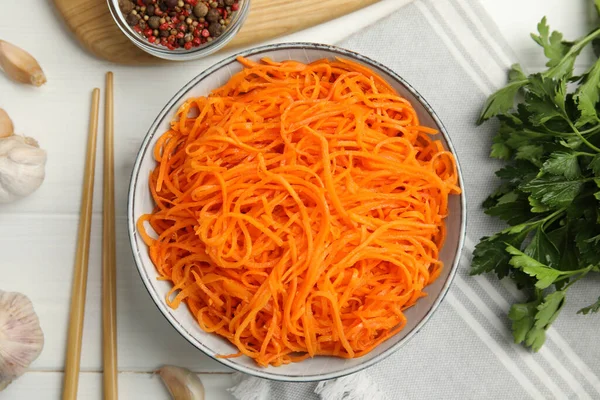 Delicious Korean carrot salad, garlic, parsley and spices on white wooden table, flat lay