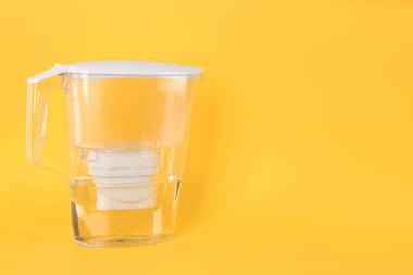 Sarı arka planda arıtılmış suyla filtre sürahisi. Metin için boşluk