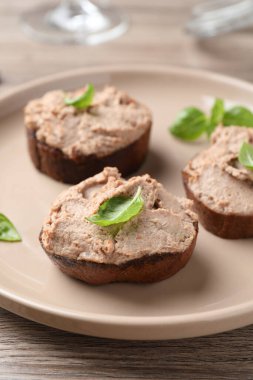 Lezzetli ezmeli ekmek dilimleri ve ahşap masada fesleğen, yakın plan.