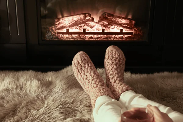 Woman in knitted socks resting near fireplace at home, closeup of legs