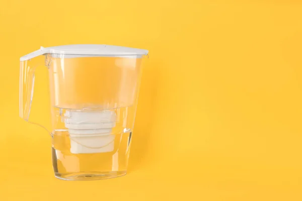 Filter jug with purified water on yellow background. Space for text