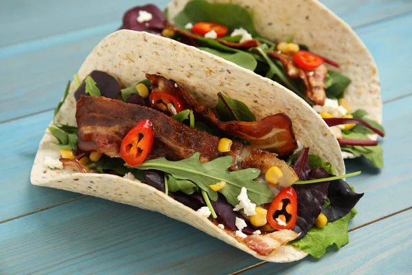 stock image Delicious tacos with fried bacon, vegetables and cheese on turquoise wooden table, closeup