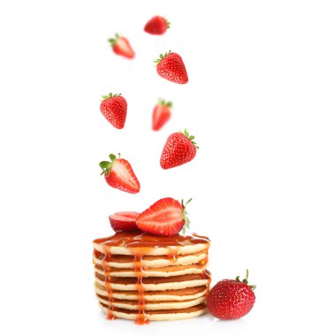 Taze çilekler beyaz arkaplana karşı istiflenmiş kreplere dökülüyor.