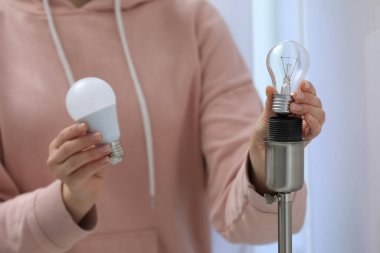 Bir kadın evdeki lambada parlak ampulü floresan lambayla değiştiriyor, yakın plan. Enerji tasarrufu kavramı