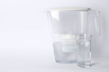 Filter jug and glass with purified water on white background. Space for text