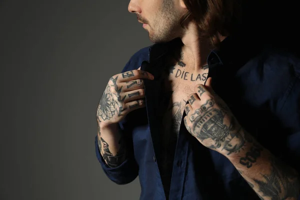 Young man with tattoos on body against black background, closeup