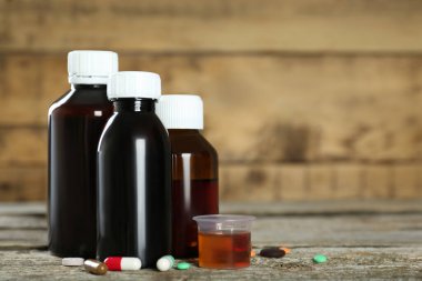 Öksürük şurubu şişeleri, ölçü kabı ve tahta masanın üzerindeki haplar. Metin için boşluk