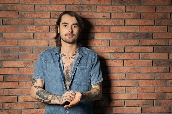 Young man with tattoos on body near brick wall