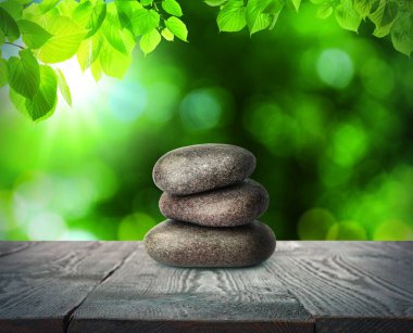 Ahşap masanın üzerine istiflenmiş taşlar yeşil yaprakların altında bulanık arka planda. Zen kavramı