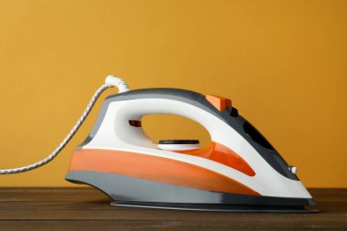 Turuncu arka plana karşı ahşap masa üzerinde modern bir ütü. Ev aletleri