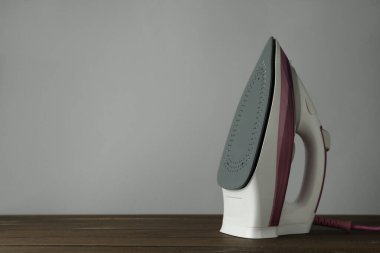 Açık gri arka plana karşı ahşap masa üzerinde modern bir ütü, yazı için yer. Ev aletleri